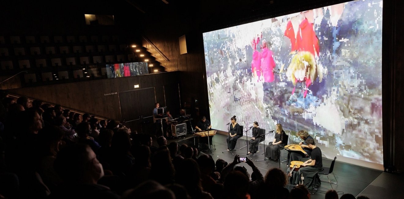 Audience watching a musical performance with abstract image in background of stage