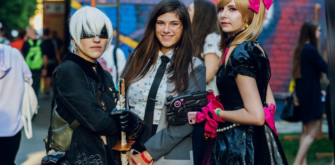 Three women dressed in fantasy and punk costumes standing in front of a mural at a festival in Kyiv