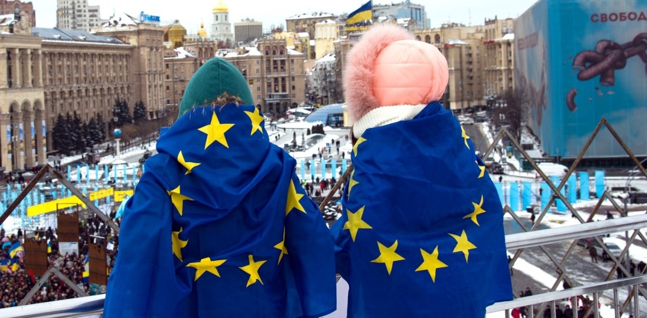 Two people overlooking square with EU flags on their backs