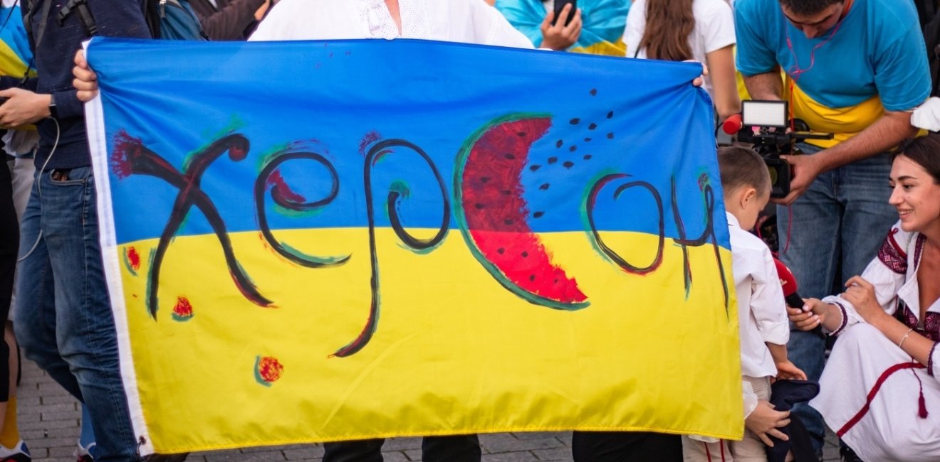 Person holding Ukrainian flag with text "Kherson" and watermelon motifs 