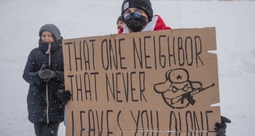Protester in snow with sign that reads "That one neighbor that never leaves you alone" and a caricature representing the Russian state