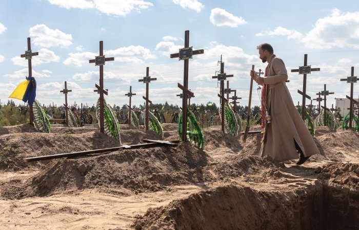 A priest overseas the burial of the remains of 13 unidentified and two identified people who were killed in the Bucha district during the Russian occupation