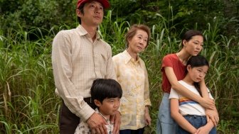 A family of five people stand in a wooded area.