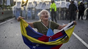 Consuelo Marquez holds a Venezuelan flag in front of police blocking demonstrations against the official election results declaring President Nicolas Maduro's reelection, the day after the vote in Caracas, Venezuela, Monday, July 29, 2024. 