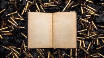 open book in a black hardcover with yellowed blank pages. Empty gun cases lying on charred coals.