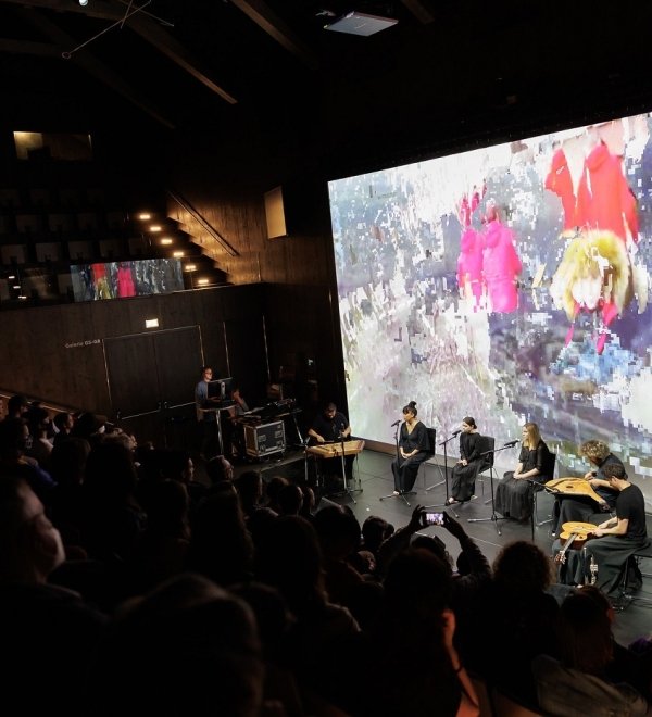 Audience watching a musical performance with abstract image in background of stage