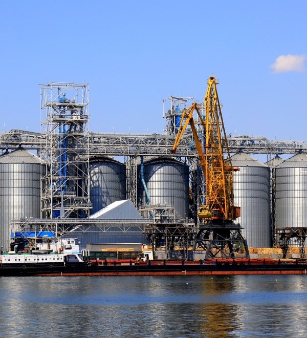 Harbor cranes unload barge at Odesa Seaport amid large metal tanks with wheat, grain, food. 