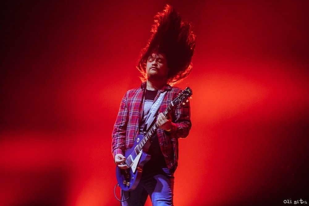 Man on stage whipping hair and playing the guitar
