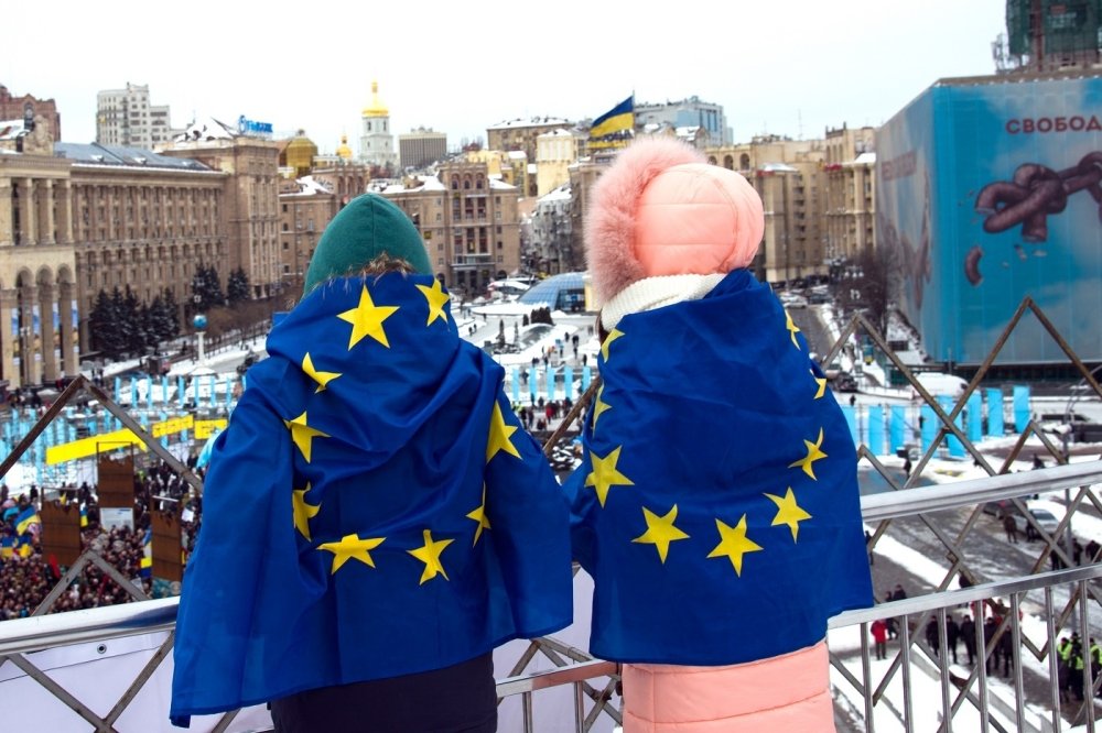 Two people overlooking square with EU flags on their backs