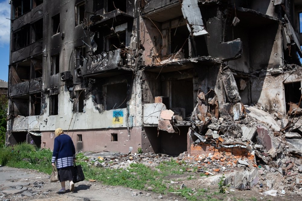 old woman walks past apartment building destroyed by the Russian army as a result of Russia's invasion of Ukraine in Borodianka, Ukraine